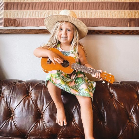 Young girl sitting on couch with ukelele after seeing pediatric dentist in Aledo